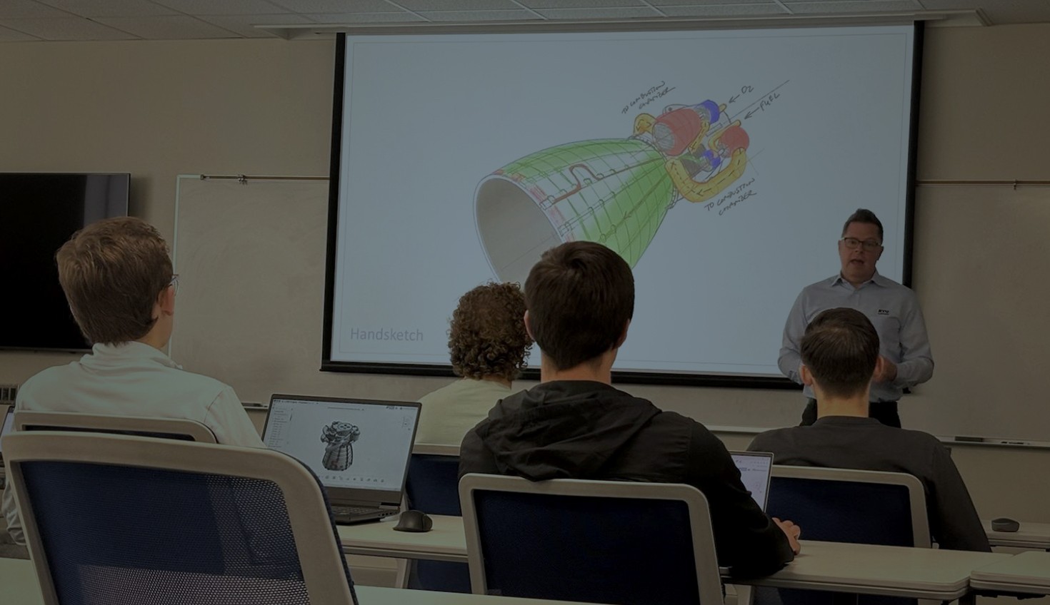 Image with an overlay showing a teacher in a STEM classroom lecturing in front of a CAD model.