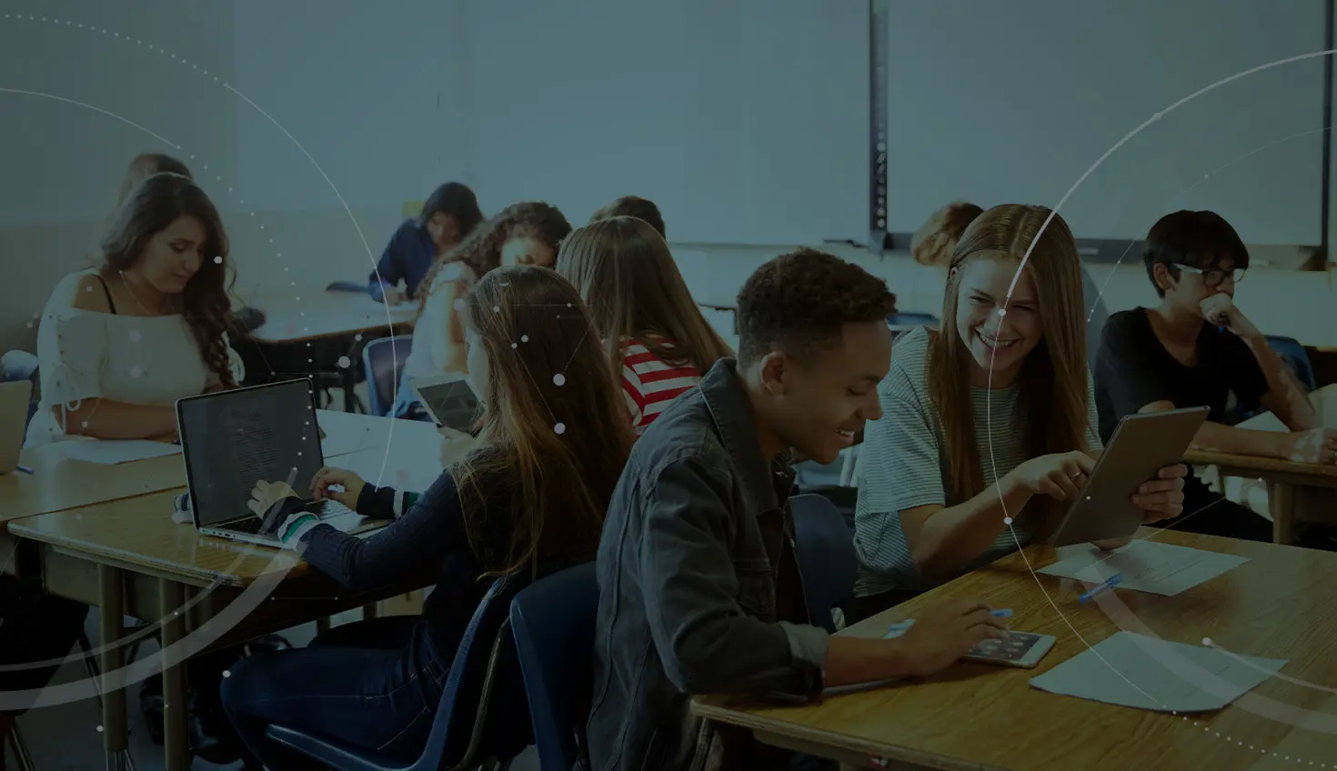 Stock image with an overlay showing students in a classroom using tablets and laptops.