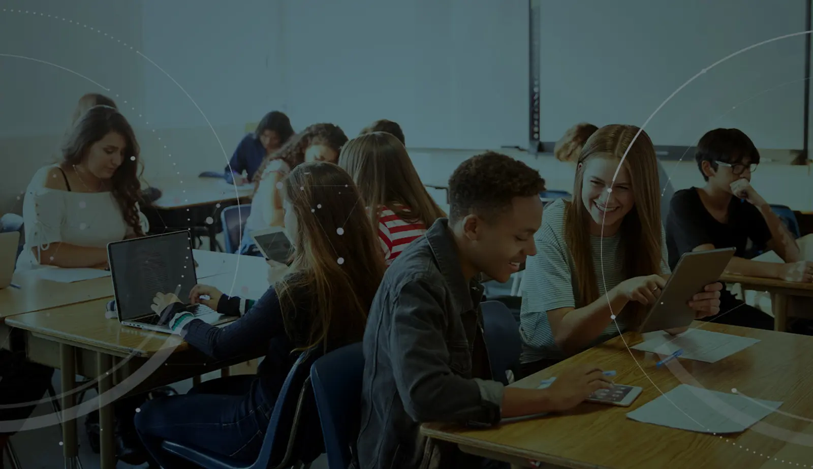 Stock image with an overlay showing students in a classroom using tablets and laptops.