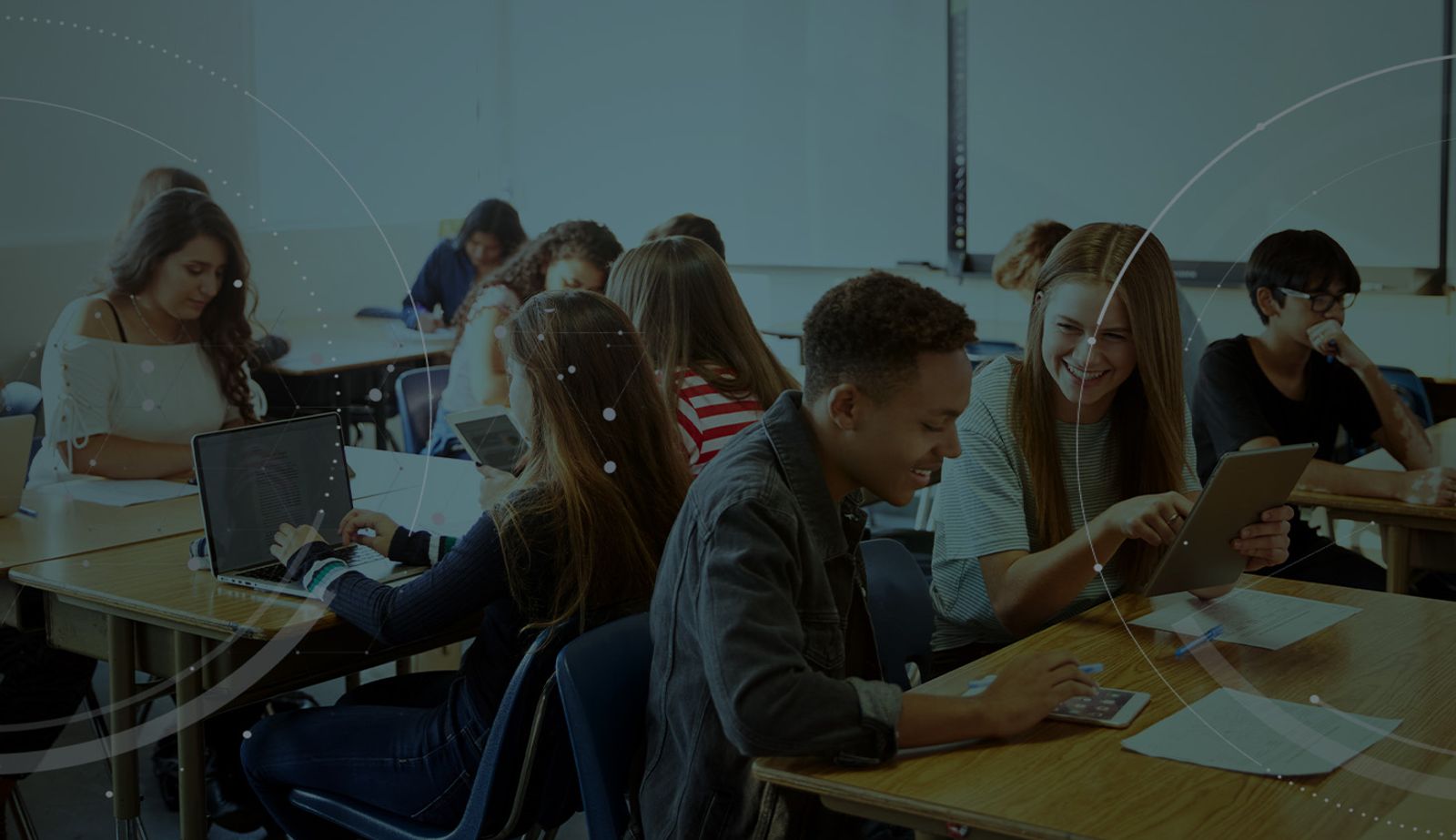 Stock image with an overlay showing students in a classroom using tablets and laptops.