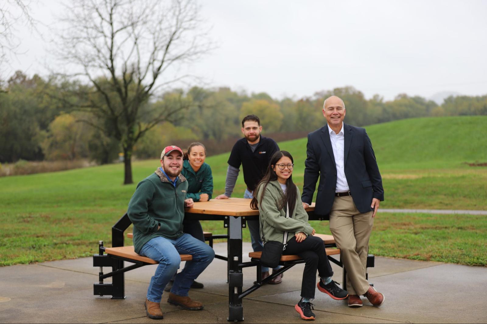 Image showing a group that helped build the picnic table they are sitting on at a park.