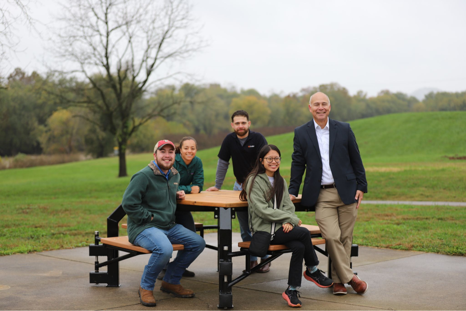Image showing a group that helped build the picnic table they are sitting on at a park.