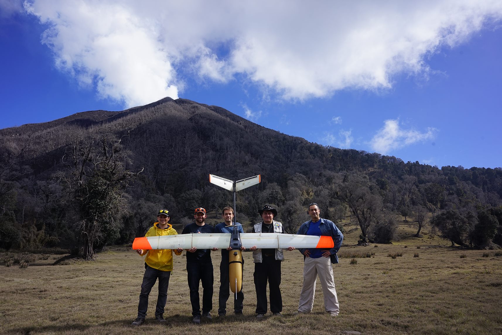 engineers posing in front of a volcano with large drone